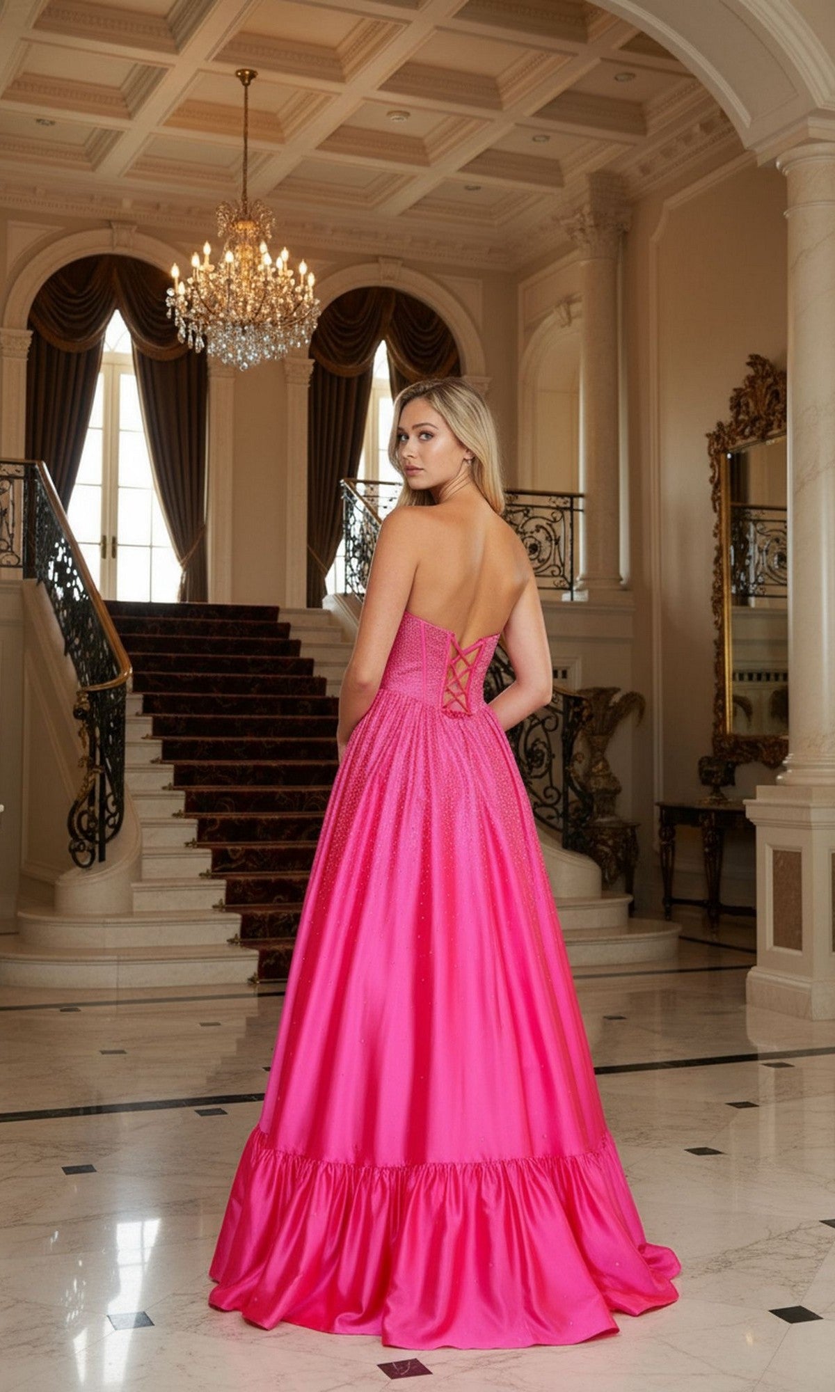 Wearing the Long Prom Dress: Poly USA 25134, featuring a strapless corset bodice and shimmering heat stone embellishments, a woman poses on a marble foyer floor with a grand staircase and glowing chandelier behind her.